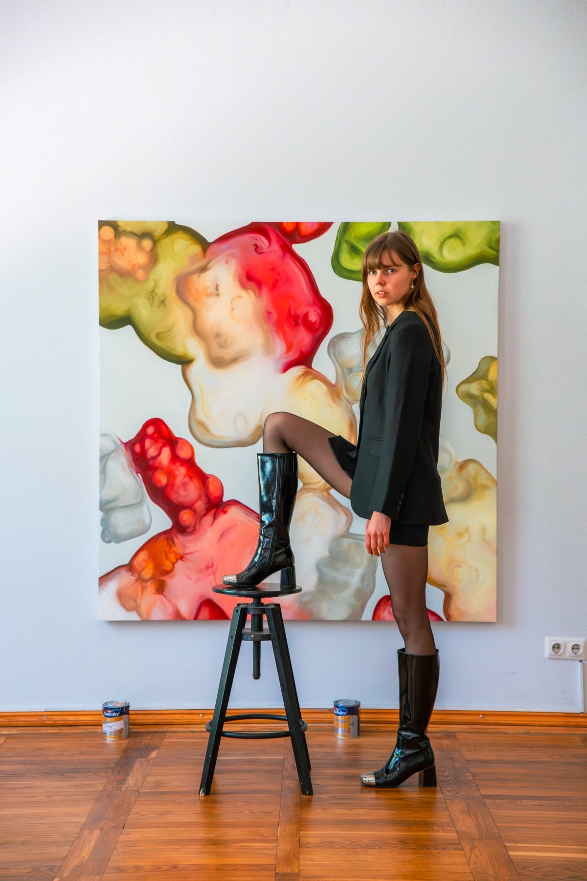 Elina Tailor standing beside her colourful painting in the studio